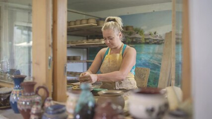 Front view of blonde woman potter making pottery on potters wheel.