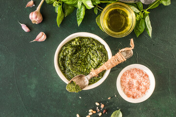 Pesto sauce in bowl with ingredients on rustic green table. Traditional Italian pesto recipe for making fettuccine, pasta, bruschetta.