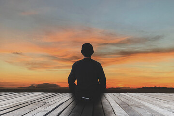 Closeup of a young asian man sitting alone on old wood bridge practicing yoga and meditate in the lotus pose outdoor in the morning for relaxation and peace of mind. Harmony and meditation concept.