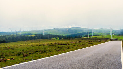 Carretera de monta&ntilde;a solitaria con un grupo de aerogeneradores eolicos entre la niebla 