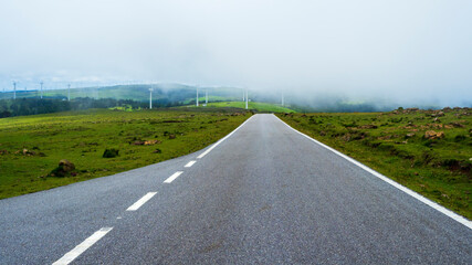 Carretera de montaña solitaria con un grupo de aerogeneradores eolicos entre la niebla 