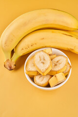 White cup with sliced bananas on a yellow background. Tropical fruits, healthy food, vitamins
