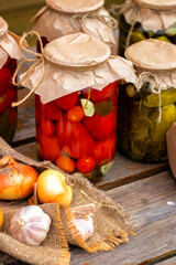 Pickled tomatoes and cucumbers in glass jars on an old wooden table. Summer harvest.