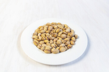 Heap of salty pistaches in  plate on white wooden table 