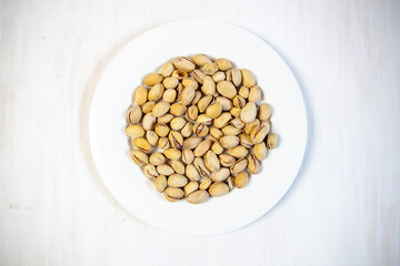 Heap of salty pistaches in  plate on white wooden table 
