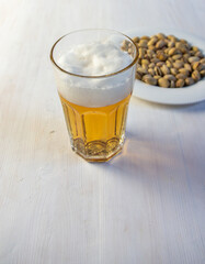Glass of light beer with foam and plate with pistaches on white background