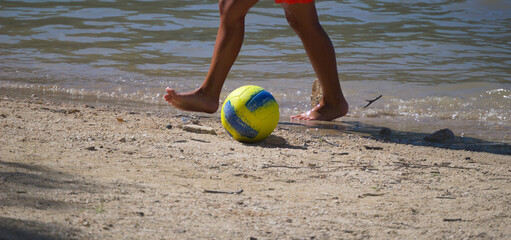 Jovem rapaz à jogar bola numa praia fluvial perto da água - juvenil