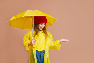 Happy girl child laughing with yellow umbrella and in the red hat on colored beige background.