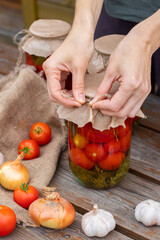 Woman cans pickled tomatoes in glass jars on an old wooden table. Summer harvest.