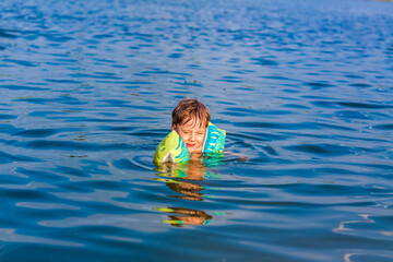 Fototapeta na wymiar A happy child is swimming in the river on a very hot summer day. Swim in reservoirs. A happy family has fun and splashes in the water in the summer.