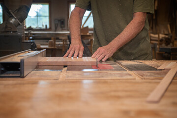 Close up of furniture maker feeding a board through a tablesaw in the woodshop - obrazy, fototapety, plakaty