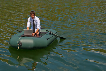 A man in a white shirt on an inflatable boat. Businessman with laptop resting on the lake. The concept of remote work, leisure and freelance.