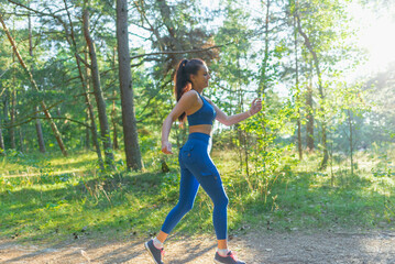 Sporty young brunette woman doing running activities.Young woman running outdoors on a sunny summer evening park.