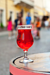 Glass of red wine close up. Alcoholic liqueur on a wooden barrel on a background of the city. Blurred people in the background.