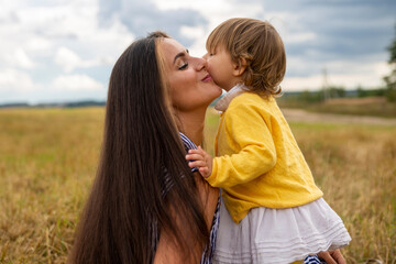 adorable toddler girl kisses her mother on a picnic in the field.