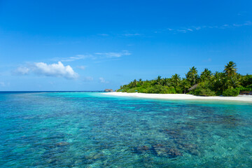 Maldives island with crystal clear sea, coral and blue sky.