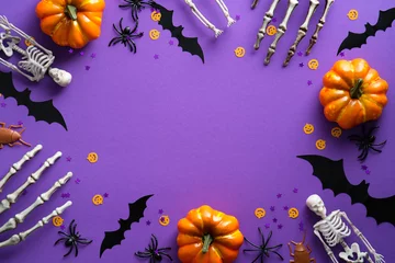 Poster Im Rahmen Halloween decorations on violet background. Flat lay pumpkins, bats, spiders, skeletons and confetti. Top view with copy space. Halloween concept. © photoguns