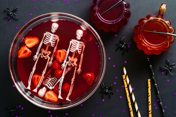 Happy Halloween holiday party composition with bowl of bloody drink, skeletons, drinking straws on black background. Flat lay, top view
