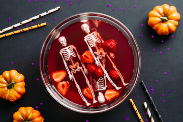 Happy Halloween holiday party composition with bowl of bloody drink, skeletons, pumpkins on black background. Flat lay, top view
