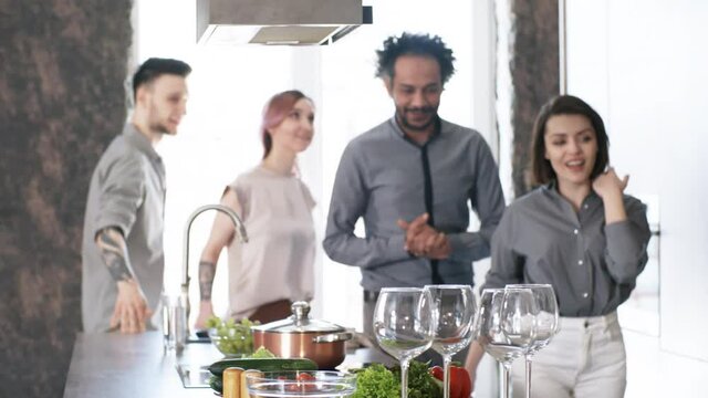 Group of joyous multiethnic friends walking into the kitchen, smiling and chatting while going to prepare food for dinner party