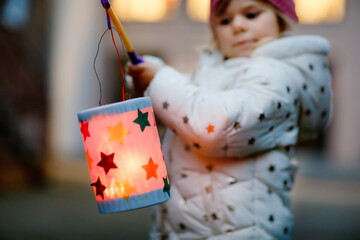 Close-up of little kid girl holding selfmade lanterns with candle for St. Martin procession. Healthy toddler child happy about children and family parade in kindergarten. German tradition Martinsumzug - obrazy, fototapety, plakaty