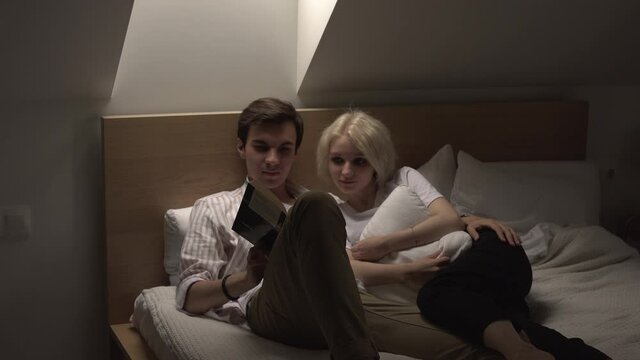 young couple in love lying in the bed and reading book