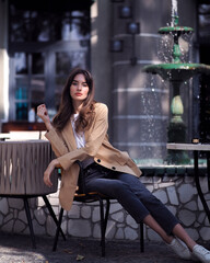 A woman sits in a summer cafe in the shade in a beige jacket