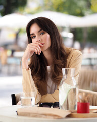 Fototapeta premium A woman on a summer terrace sits at a table in a beige jacket