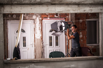 Behind the scene. Filmmaking lighting technician electric engineer adjusting reflector and setup...