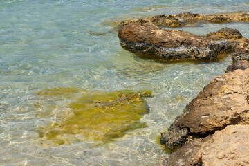 Surface of clear water on tropical sandy beach with stones in Crete Greece.