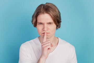 Guy in white T-shirt put finger lips shows sign silence isolated on blue background