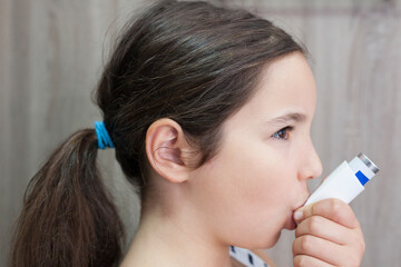 Child girl using medical spray for breath. Inhaler
