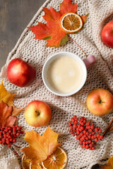 Autumn mood flat lay with cup of coffee, fallen leaves, red berries, apples, warm knitted blanket and cinnamon. Autumn holidays, thanksgiving day, home weekend. Flat lay, top view, copy space.