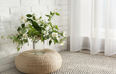 Bouquet of beautiful jasmine flowers in glass vase near white brick wall indoors, space for text