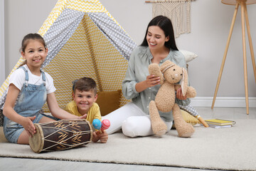 Mother and children playing near toy wigwam at home © New Africa