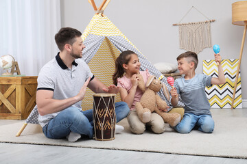 Father and children playing near toy wigwam at home © New Africa