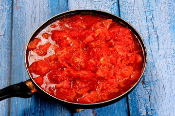 Closeup of boiling chopped red tomatoes sauce in a pan on the stove, blue wooden board background. Blanched tomatoes 