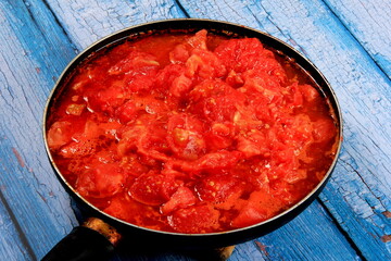 Closeup of boiling chopped red tomatoes sauce in a pan on the stove, blue wooden board background. Blanched tomatoes 