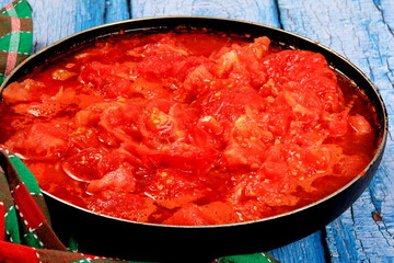 Closeup of boiling chopped red tomatoes sauce in a pan on the stove, blue wooden board background. Blanched tomatoes 
