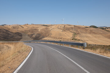 Alta Irpienia, windy hills in full sun. Summer, wheat fields, asphalt ribbon curving towards the sky. Italy, Campania.