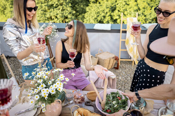 Young group of stylish people having a festive dinner on the roof terrace. Friends hanging out together, drinking wine and talking outdoors