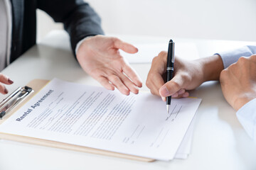 Close-up man hand signing home loan contract purchase agreement document with property real estate agent