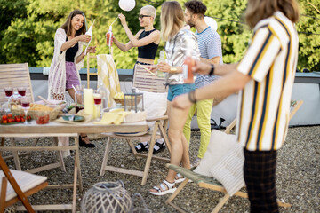 Young group of stylish people having a festive dinner on the roof terrace. Friends drinking beer and hanging out at picnic