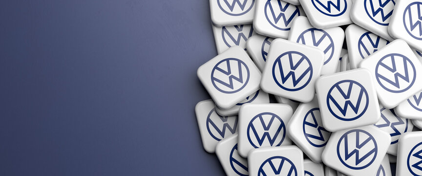 Logos of the German mass car manufacturer Volkswagen VW on a heap on a table. Copy space. Web banner format.