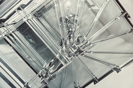 Contemporary metal winding stairs with clear glass steps installed in spacious light hall in building close bottom view