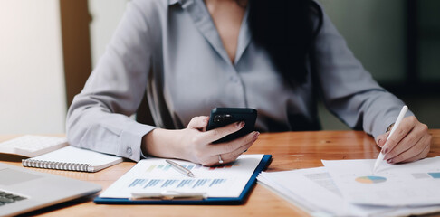 close up view of hands women using smartphone and laptop analyzed financial statements, business document, chart and graph paper, marketing report, accounting, investor, work from home concept.