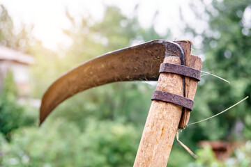 Old rusty scythe on wooden handle on blurred background with bokeh effect in yard of country house in summer extreme closeup