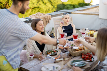 Sad and thoughtful woman sitting separately on a party with friends outdoors, young people dining on a rooftop terrace