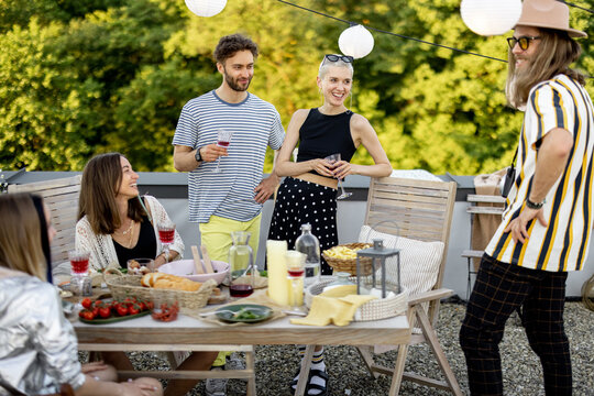 Young Group Of Stylish People Having A Festive Dinner On The Roof Terrace. Friends Hanging Out And Having Great Summertime Together Outdoors