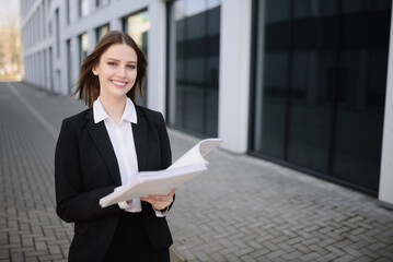 A confident business woman stands with documents near the business center.